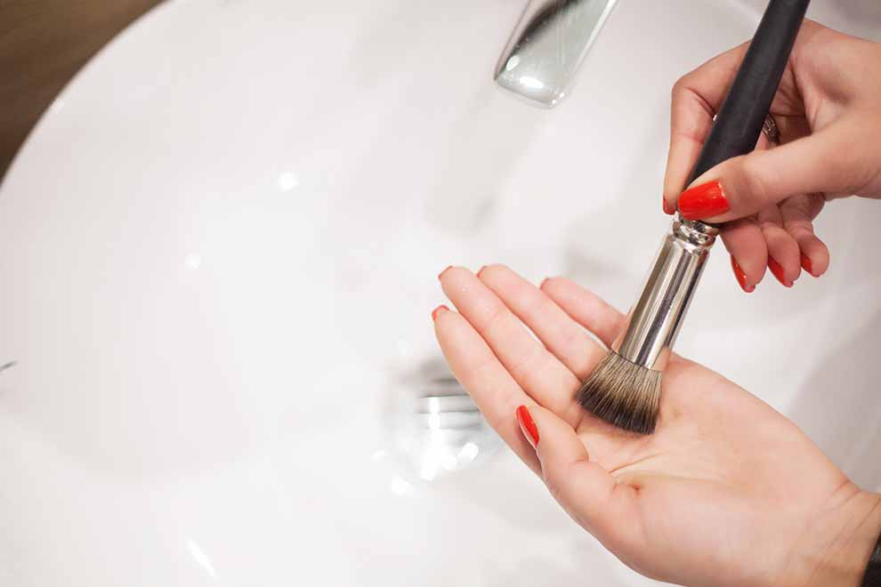 mulher lavando seus pinceis com sabão na pia do banheiro 