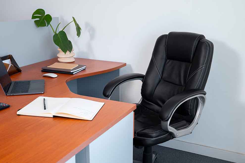 móveis confortáveis e ergonómicos de escritório com um notebook, uma caderneta e uma caneta em cima de uma mesa e com uma parede branca e chão com tapete cinza