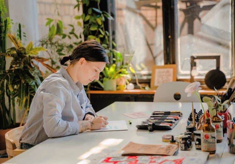 Como organizar os materiais e fermentas do atelier Mulher escrevendo em cima de uma mesa.