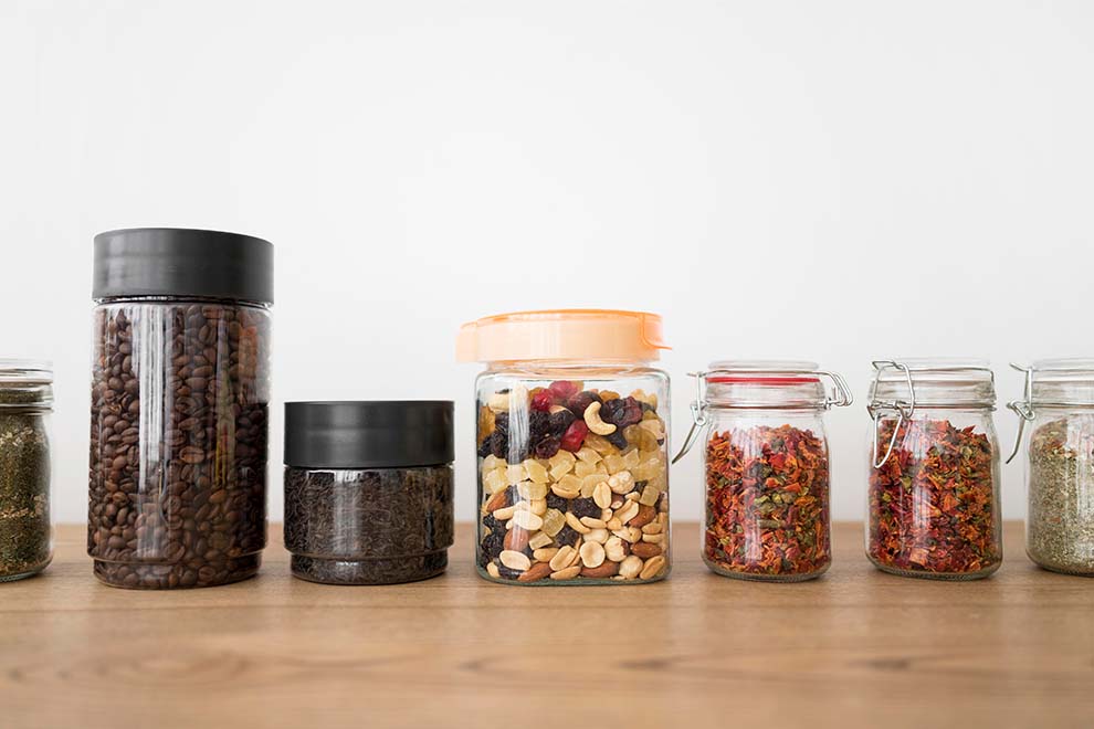 vários potes em acrílico com grãos e temperos dentro em cima de uma mesa de madeira levemente escura