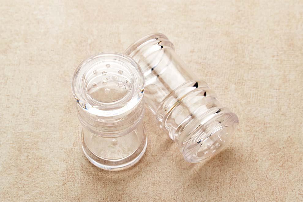 um saleiro e um moedor de pimenta de acrílico vazios em cima de uma superfície plana na cor bege