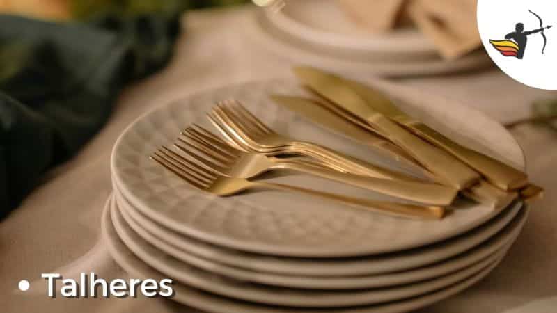 Conjunto de pratos brancos em cima de mesa com talheres de cor dourada.
