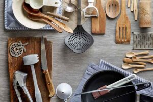 vários utensílios de cozinha em cima de uma mesa cinza de madeira e alguns panos de cozinha em azul acinzentado e branco