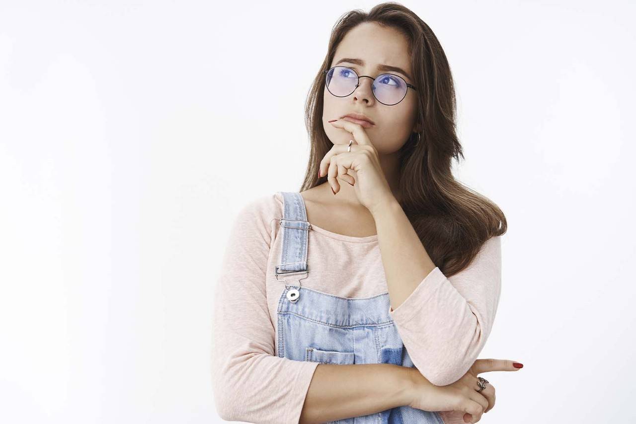 Modelo feminina em pé, em pose de reflexão, em um fundo branco. 