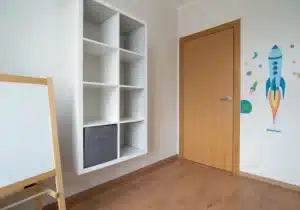 quarto de solteiro com um adesivo na parede e com uma prateleira e do lado um quadro de pintar