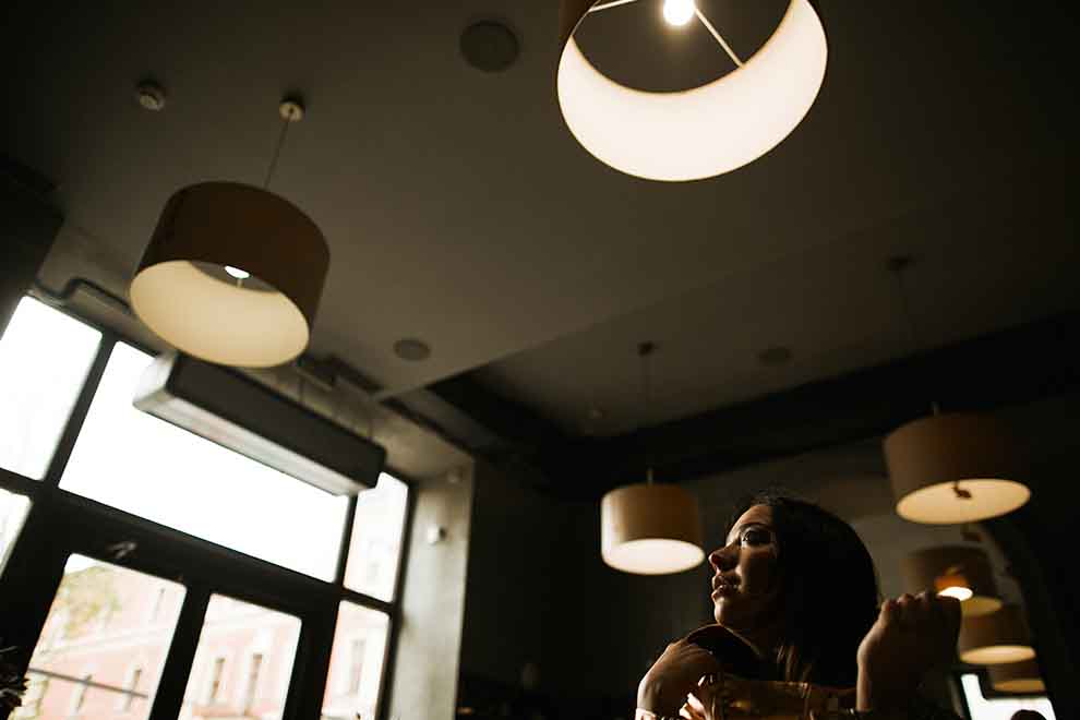 Mulher contemplativa sob luzes pendentes em café