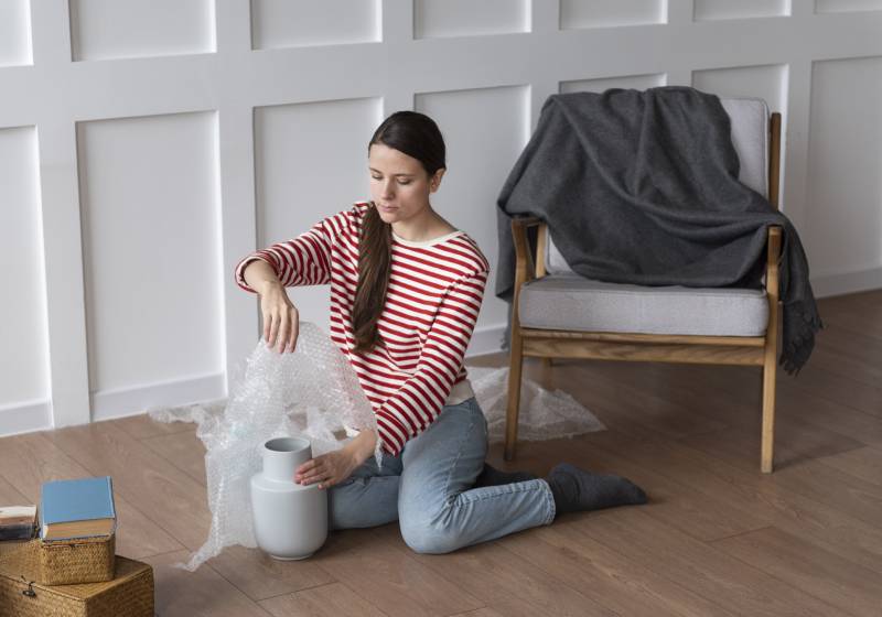 Modelo sentada no chão embando um vaso.