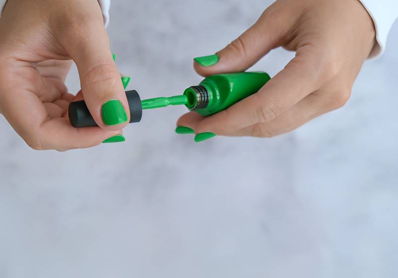 Uma pessoa passando esmaltes nas unhas da cor verde