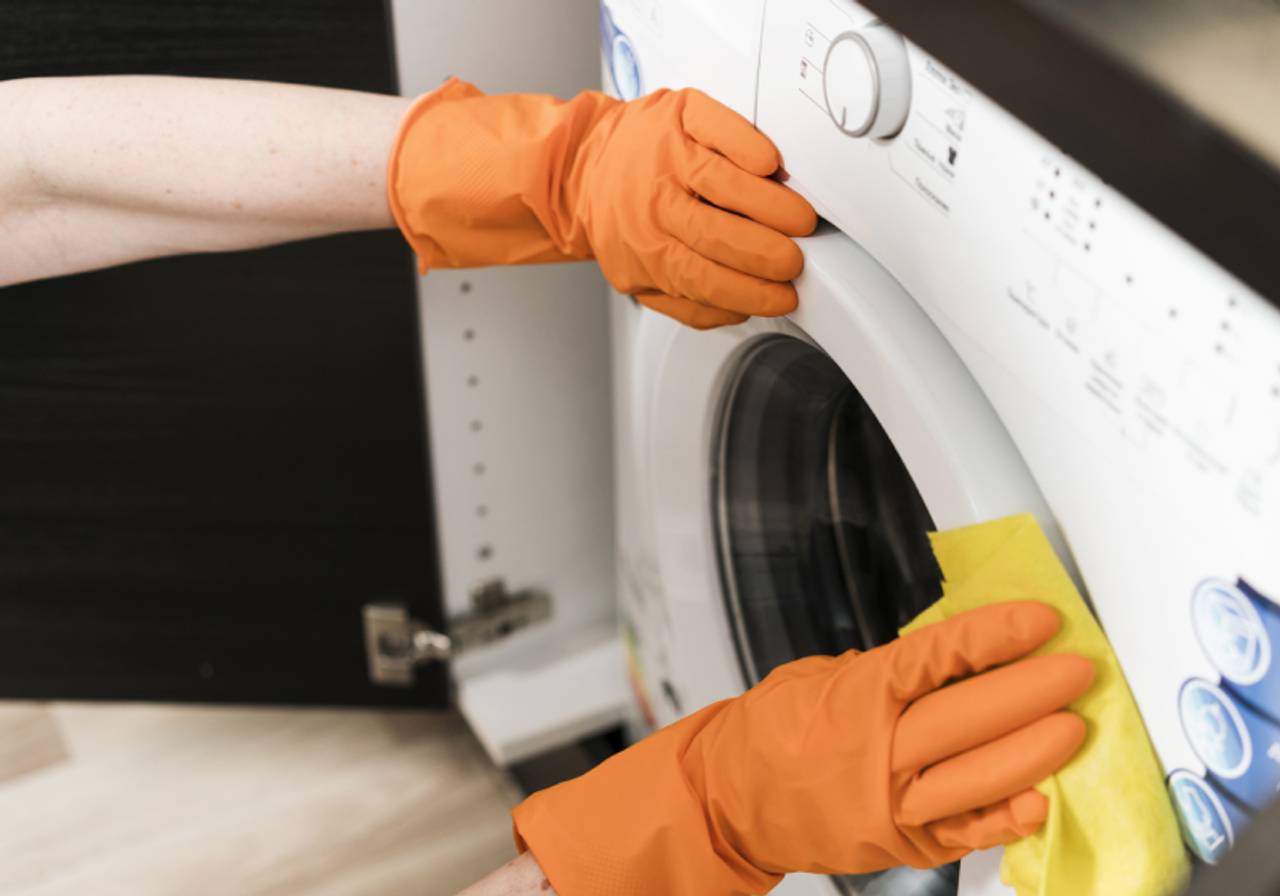 ângulo de cima de mulher limpando maquina de lavar com luva e pano