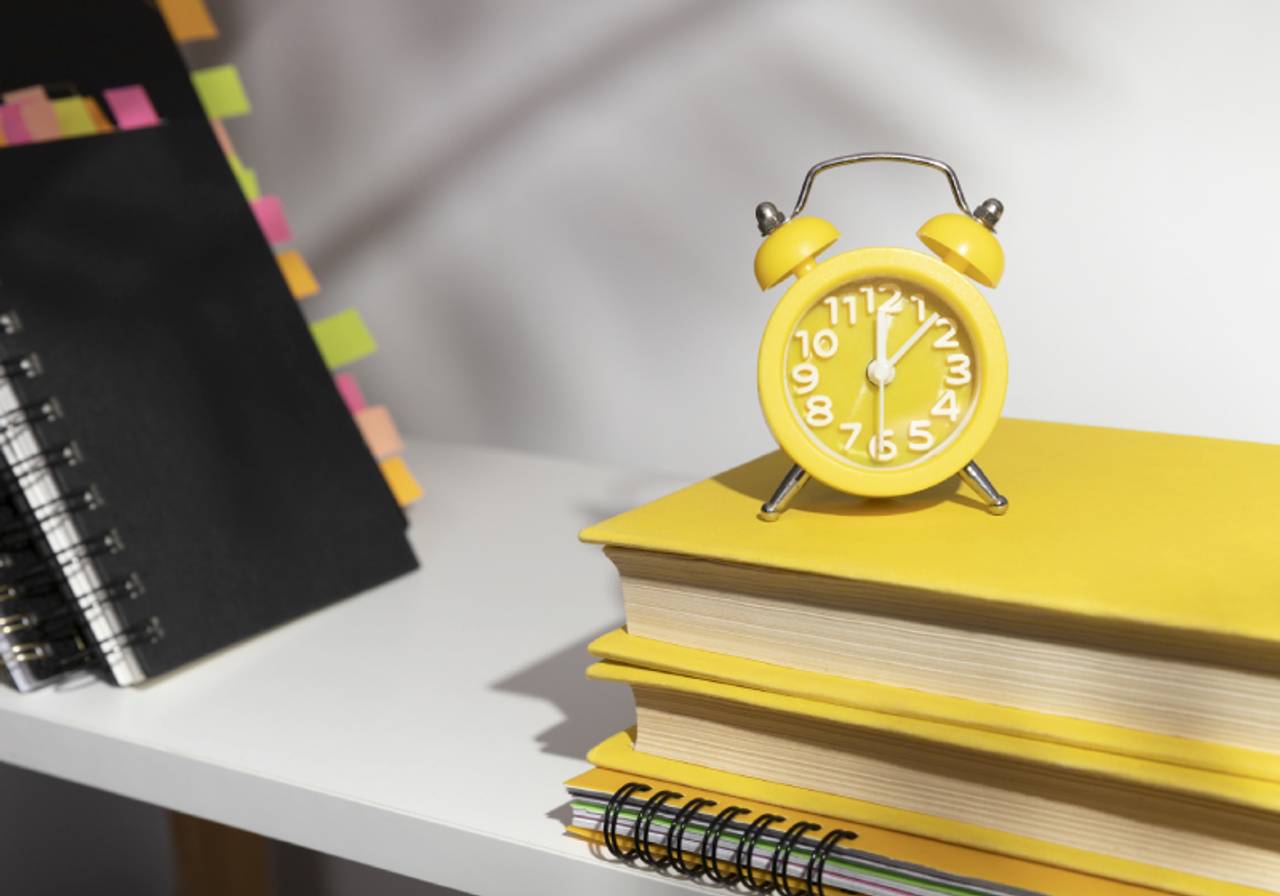 prateleira com livros e despertador amarelo encima de livros