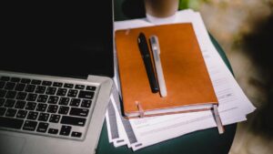 Agenda em uma mesa, em cima de papéis e um notebook do lado.