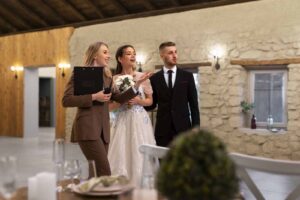 Imagem de uma organizadora de casamento com os noivos ao lado em um salão de festa