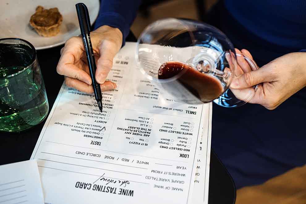 uma pessoa segurando uma taça de vinho enquanto anota o que tera no chá de casa nova em formato de lista 