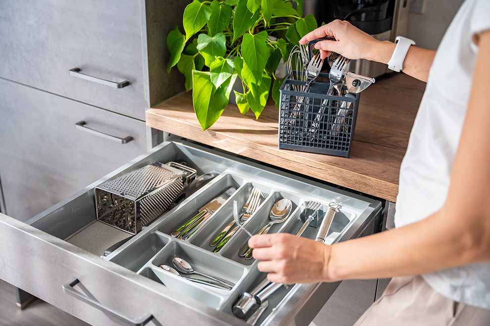 Mulher organizando a gaveta da cozinha com os talheres em um dia ensolarado.