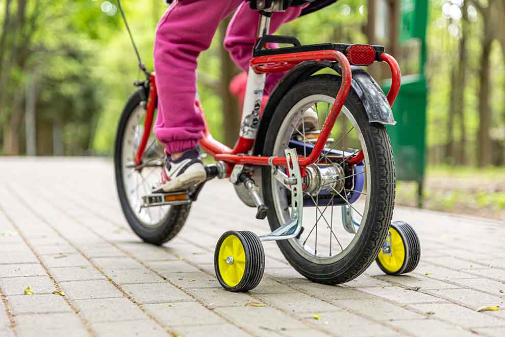 Criança pedalando uma bicicleta com rodinhas de apoio