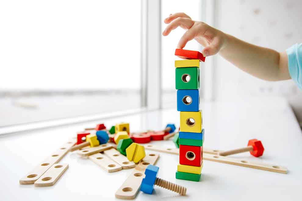 Criança empilhando blocos de madeira coloridos.