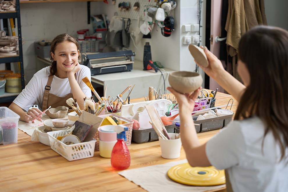 Duas mulheres sorrindo enquanto moldam cerâmica