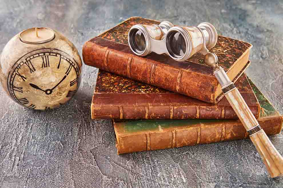 Livros antigos com lunetas e um relógio decorativo.