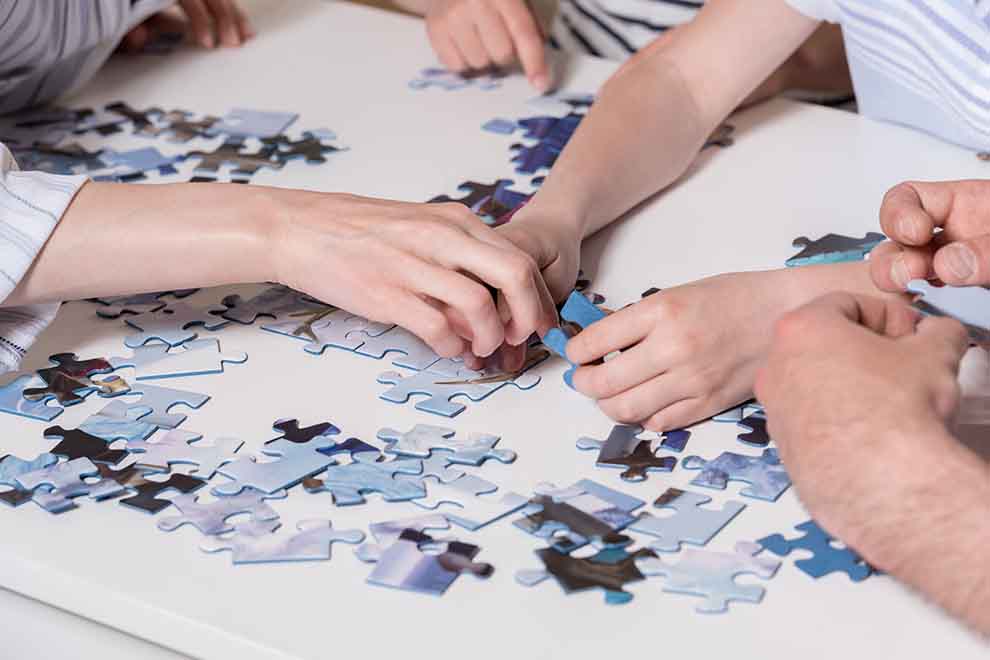 Várias mãos montando um quebra-cabeça colorido.