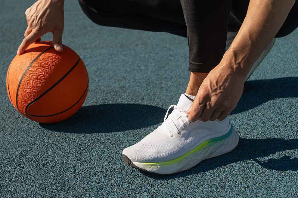 Pessoa amarrando tênis ao lado de bola de basquete.