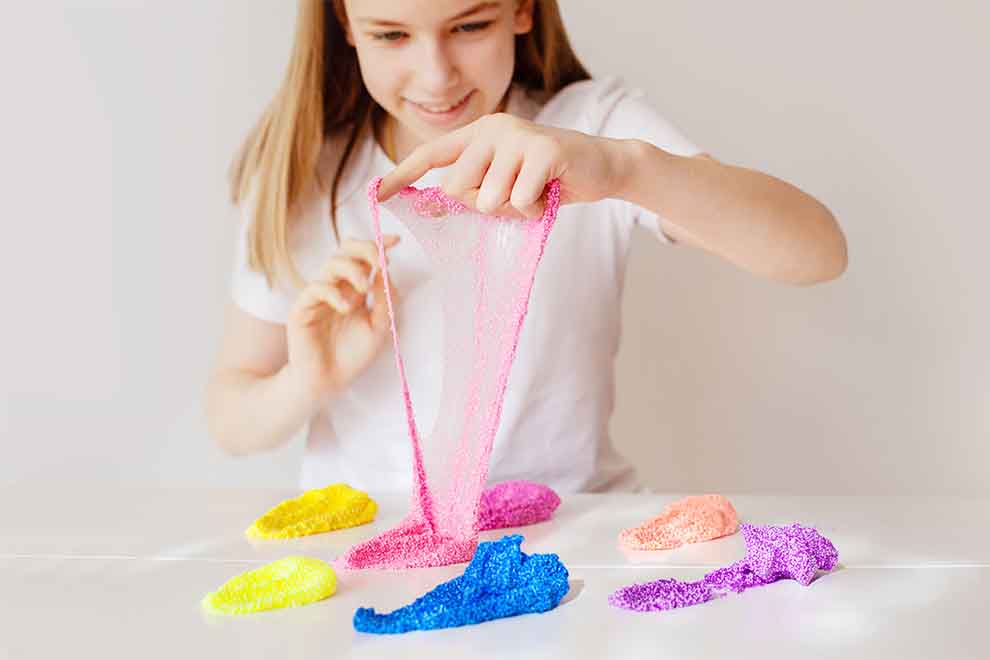Adolescente brincando com slime colorido em cima de uma mesa branca em um fundo branco.