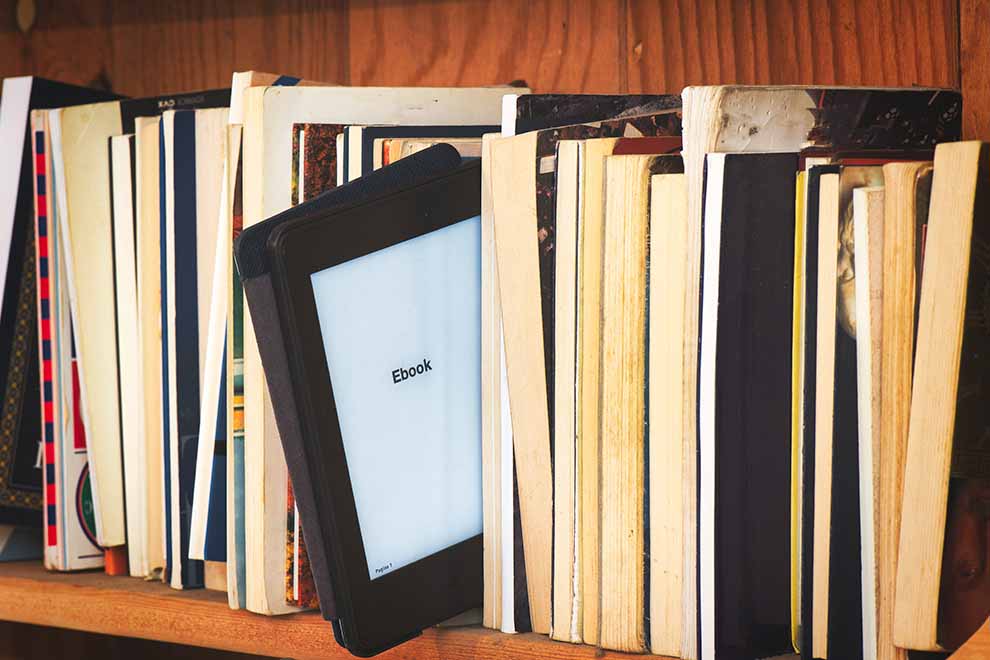 Estante de livros com um kindle de e-book entre os livros fisicos em uma biblioteca.
