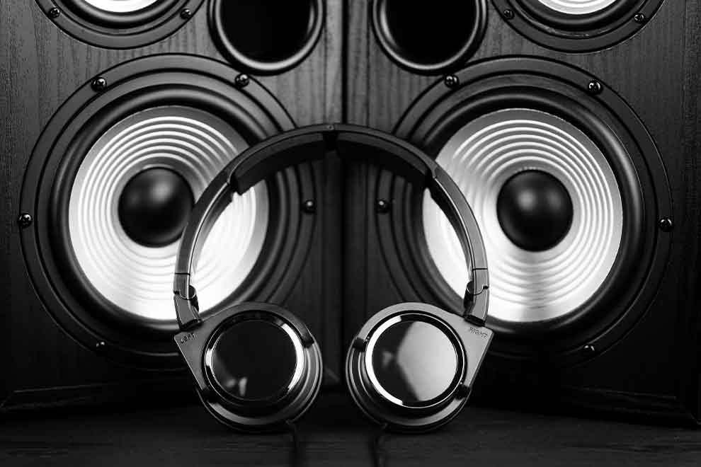 Fone de ouvido na frente de uma grande caixa de som ambas pretas.