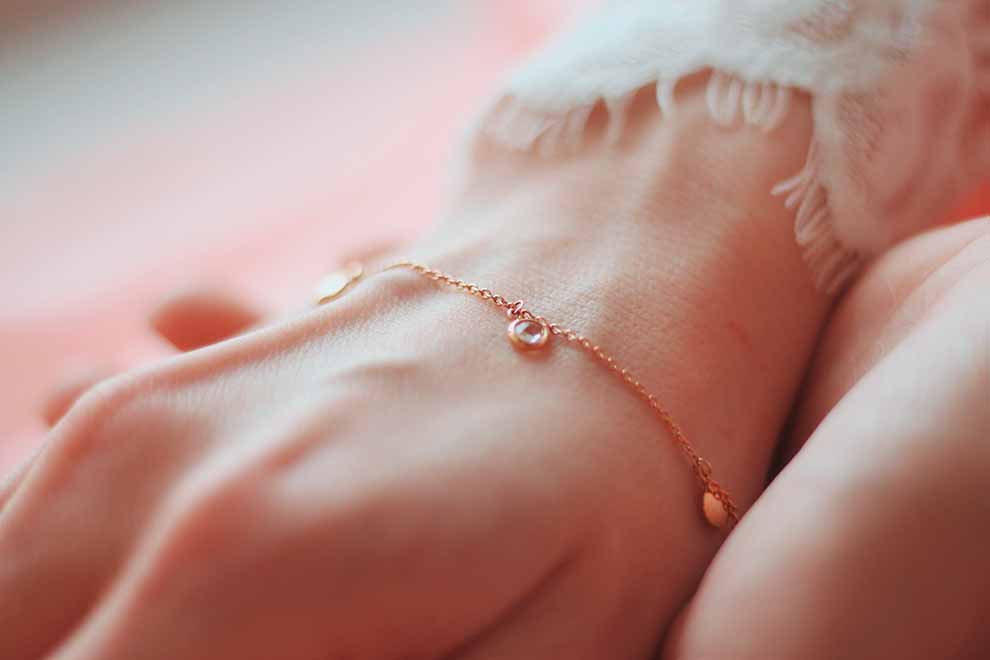 Mulher usando uma pulseira delicada em um fundo rosa claro.