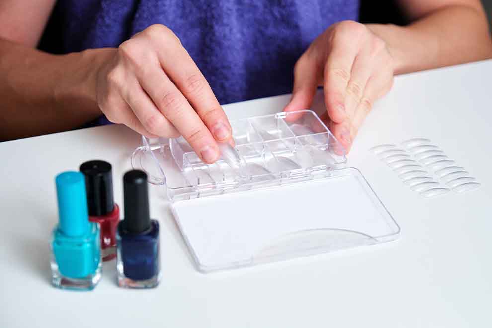 Pessoa organizando unhas postiças com esmaltes ao lado