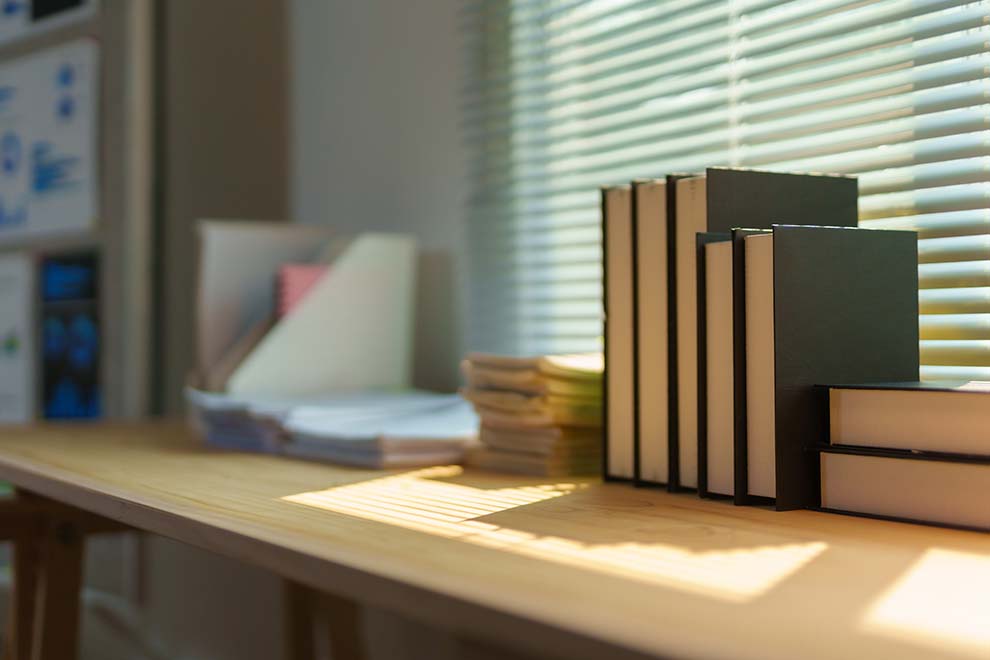 Mesa com livros e papéis organizados sob luz natural.